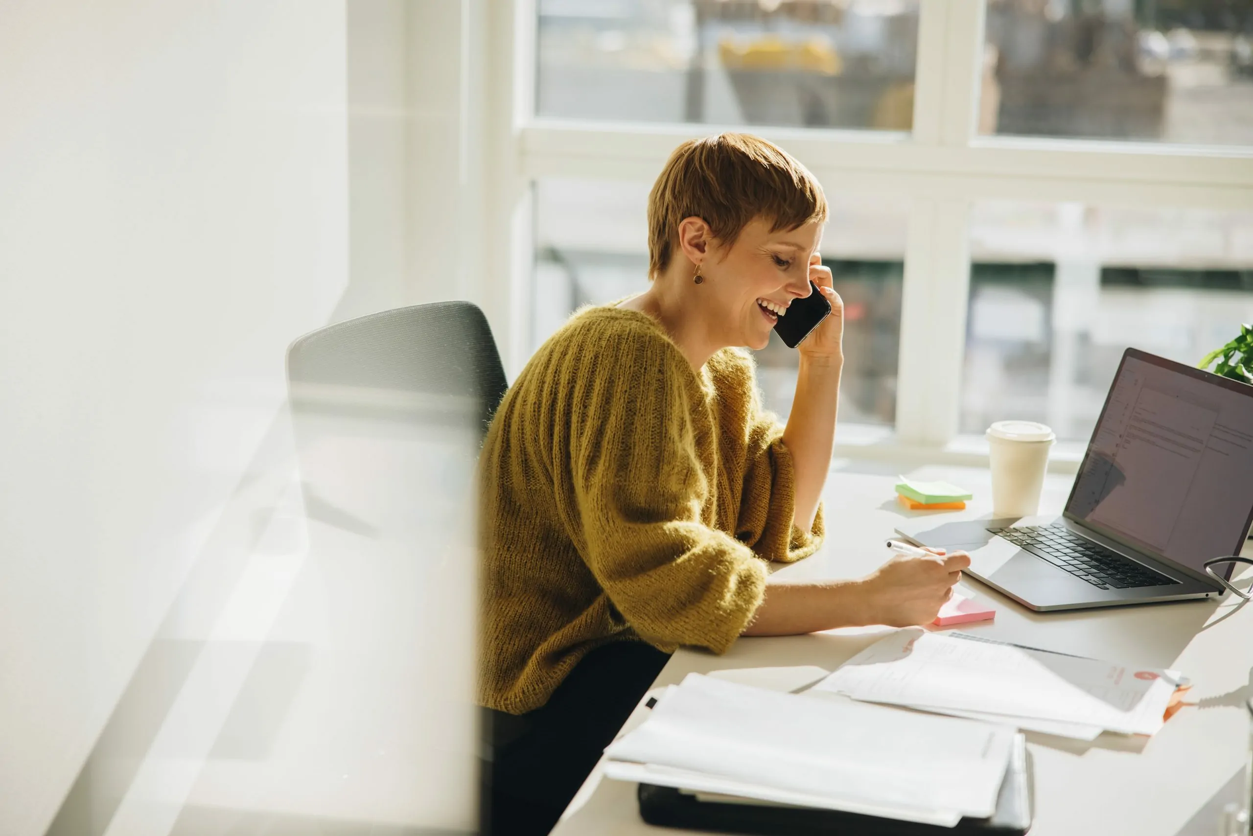 woman in office wearing a yellow jersey with short hair on her phone in the office that is using mobile device management software on the device