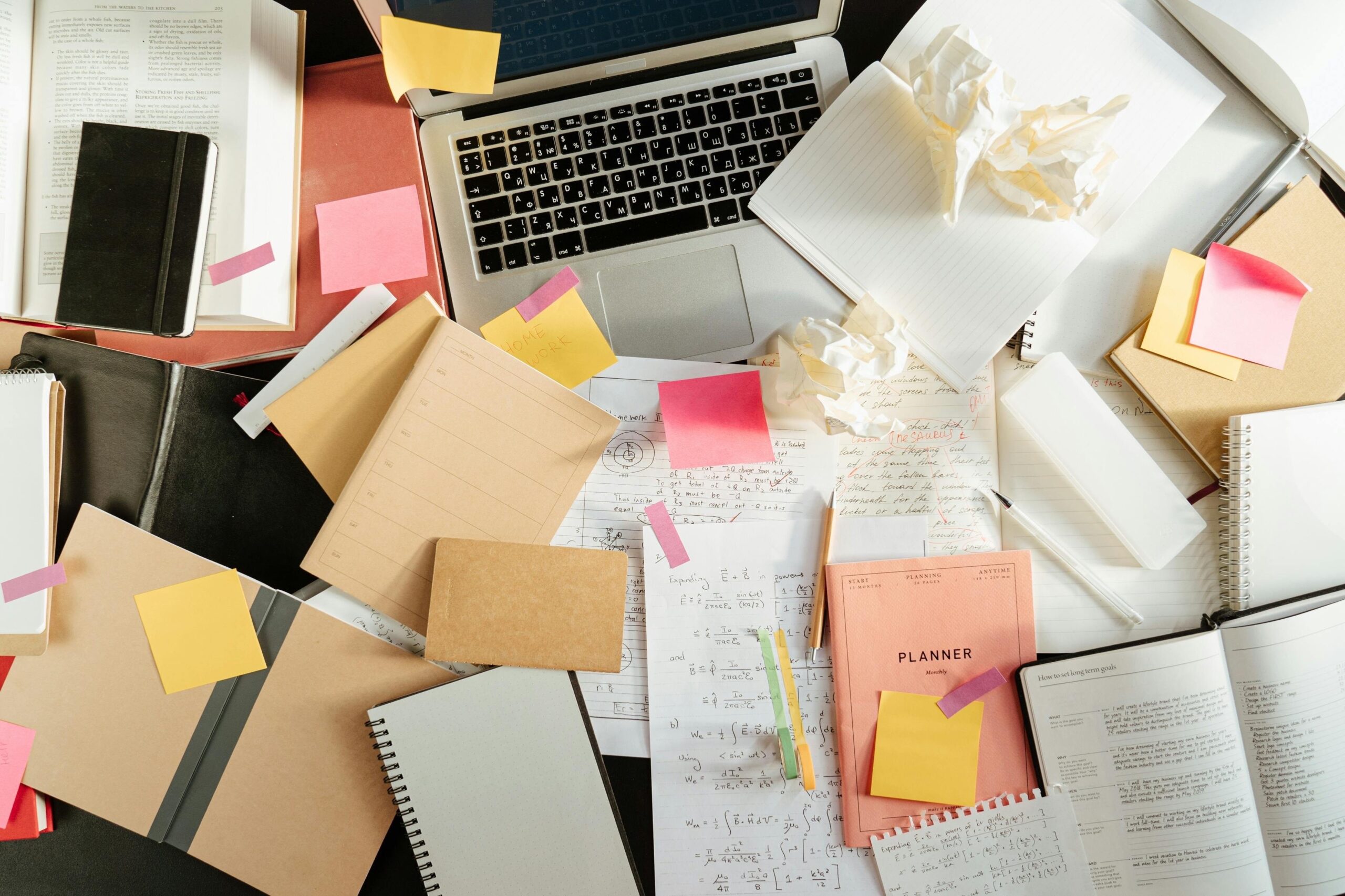 An IT Administrator's untidy desk with a laptop and lots of post-it notes
